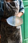 Coltivare artigiano irriconoscibile in grembiule dimostrando piatto creativo in ceramica in officina — Foto stock