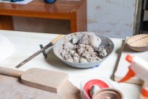 From above bowl with soft clay placed on wooden table near set of potter tools in workshop — Stock Photo