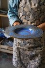 Cultivar artesão irreconhecível em avental demonstrando placa de cerâmica criativa em oficina — Fotografia de Stock