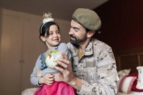 Desde abajo de soldado positivo hablando con hija y señalando el lugar en el globo antes de ir a servir en el ejército - foto de stock