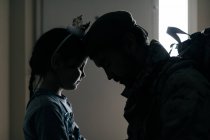 Seitenansicht Silhouette eines aufgebrachten Mädchens, das Papa mit der Stirn berührt, während Papa in den Krieg zieht — Stockfoto