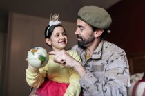 Desde abajo de soldado positivo hablando con hija y señalando el lugar en el globo antes de ir a servir en el ejército - foto de stock