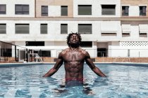 Hombre afroamericano despreocupado de pie con los ojos cerrados en la piscina y disfrutando de las vacaciones de verano - foto de stock