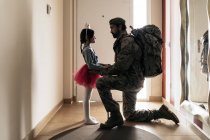 Вид збоку повне тіло солдата в камуфляжі, що стоїть на колінах перед військовою службою з маленькою дівчинкою — стокове фото