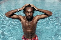 Обережно, африканський американець стоїть з закритими очима в басейні і руками на голові, насолоджуючись літньою відпусткою.. — стокове фото