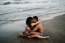 Vista lateral do jovem conteúdo descalço casal multirracial abraçando na praia do oceano arenoso durante a viagem de verão — Fotografia de Stock