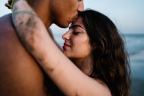 Anonymous African American male traveler kissing sincere female partner standing against ocean during summer trip — Stock Photo