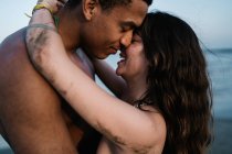 Афро-американский путешественник целует искреннюю партнершу, стоящую против океана во время летней поездки — стоковое фото