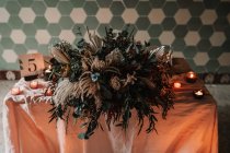 Fiori in fiore sulla tovaglia con numero e candele accese contro la parete ornamentale durante l'evento festivo in mensa — Foto stock