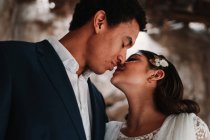 Вид збоку романтична етнічна молода пара в елегантному одязі, ніжно поєднуючись з очима, закритими у світлій весільній студії — стокове фото