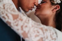 Vue latérale d'un couple romantique, jeune marié et méconnaissable, vêtu de vêtements élégants, collant tendrement les yeux fermés dans un studio de mariage lumineux — Photo de stock