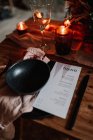 From above of paper sheet with menu list near bowl on textile and burning candles during festive occasion in cafe — Stock Photo