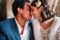 Crop giovane felice coppia di sposi che indossa abiti da sposa eleganti seduti sul pavimento faccia a faccia — Foto stock