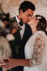 Seitenansicht von liebenden jungen ethnischen Brautpaar tragen schicke Hochzeitskleider umarmen und küssen sanft in veralteten verbleibenden Gebäude — Stockfoto