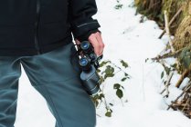 Gestutzter, bis zur Unkenntlichkeit verkleideter männlicher Wanderer in warmer Kleidung steht mit Fernglas im verschneiten Winterwald — Stockfoto