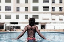 Carefree African-American man on his back in the pool and enjoying summer vacation. — Stock Photo