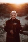 Viandante anziana in abiti casual in piedi su un molo di legno sulla spiaggia di sabbia e godersi il paesaggio marino al tramonto — Foto stock