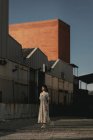 Молода етнічна леді з довгим темним волоссям у повсякденному одязі, що стоїть на вулиці біля старих будинків і дивиться в сонячний день — стокове фото