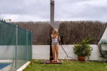 Carino bambina in costume da bagno a piedi e irrigazione prato verde dal tubo durante le vacanze estive in campagna — Foto stock
