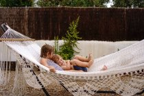 Мила босоніж маленька сестра і брат обіймаються, лежачи в гамаку і розважаючись під час літніх канікул — стокове фото