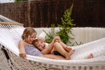 Cute barefooted little sister and brother hugging while lying in hammock and having fun during summer holidays — Stock Photo