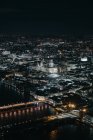 Pintoresca vista de drones de puentes sobre el río que fluyen a través de la ciudad de Londres con edificios iluminados y calles por la noche - foto de stock