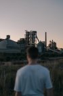 Back view of anonymous blurred male on meadow against power station under gray sky in evening field — Stock Photo