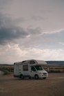 Motorhome parked on sandy terrain against rock cloudy sky in daytime — Stock Photo