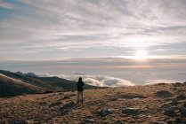 Vista trasera de explorador irreconocible turista masculino en ropa interior cálida con mochila de pie contemplando la montaña bajo densas nubes al amanecer - foto de stock