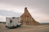 Camping-car stationné sur un terrain sablonneux contre la roche avec une surface cahoteuse sous un ciel nuageux en journée — Photo de stock