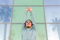 Selbstbewusste junge ethnische Athletin in stylischer Sportbekleidung schaut weg, während sie vor einem modernen Glasbau an der Stadtstraße steht — Stockfoto