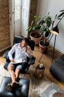 Geschäftsmann sitzt im Sessel und macht sich Notizen im Büro, während er mit dem Smartphone spricht und Nachrichten checkt — Stockfoto