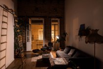 Интерьер гостиной с зелеными растениями горшок и удобный диван в квартире в мансарде стиле ночью — стоковое фото