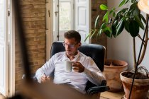 Uomo d'affari serio seduto in poltrona a casa e scrivere piani in organizzatore mentre si gode il caffè durante la pausa — Foto stock