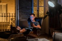 Empreendedor masculino ocupado sentado em poltrona e trabalhando no projeto enquanto usa laptop e smartphone — Fotografia de Stock