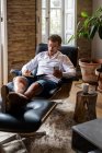 Geschäftsmann sitzt im Sessel und macht sich Notizen, während er im Smartphone surft und Nachrichten checkt — Stockfoto