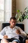 Empresário sentado em poltrona e tomar notas no organizador enquanto navega smartphone e verificação de mensagens — Fotografia de Stock