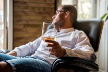 Богатый мужчина отдыхает в удобном кожаном кресле с бокалом белого вина и смотрит в раздумьях — стоковое фото