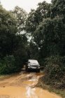 Modern SUV car driving along dirty road between green trees during road trip — Stock Photo