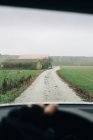 Анонимный мужчина за рулем автомобиля по пустой сельской дороге в сторону зеленого леса во время дорожной поездки — стоковое фото