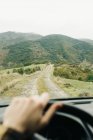 Анонімний чоловічий туристичний автомобіль на порожній сільській дорозі до зелених пагорбів під час дорожньої подорожі — стокове фото