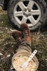 Recorte viajero masculino anónimo en botas sentadas en el suelo con tazón de macarrones durante el viaje en la naturaleza - foto de stock
