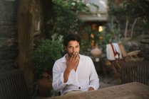 Giovane ragazzo dai capelli scuri fuma un sigaro mentre è seduto su un patio — Foto stock
