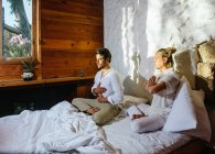 Два друга сидят на кровати, практикуя медитацию — стоковое фото