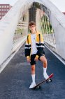 Adolescente caucasico in piedi con uno skateboard nel mezzo del ponte in città — Foto stock