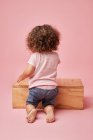 Rückansicht eines nicht wiederzuerkennenden barfüßigen Kindes in T-Shirt und Jeanshose mit lockigem Haar, das auf einer Holzplattform spielt — Stockfoto