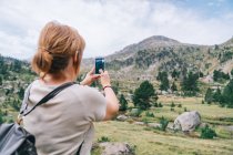 Voltar ver anônimo mochileiro feminino tirar fotos no smartphone de incríveis planaltos verdes pedregosos em Ruda Valley em Pirinéus catalães — Fotografia de Stock