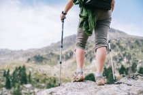 Caminante femenina anónima recortada en ropa casual con mochila con bastones nórdicos mientras está de pie en la cima de una colina pedregosa en el valle montañoso de Ruda en los Pirineos Catalanes - foto de stock
