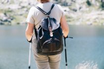 Back view anonymous female hiker standing with walking poles on stony river coast in Catalan Pyrenees on sunny summer weather — Stock Photo