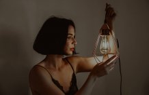 Vue latérale de délicate lanterne en métal éclairé féminin tout en étant assis dans la chambre à la maison — Photo de stock